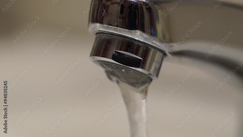 Clean water flowing from a shiny water tap, with a man reflected on it Clean water flowing from a shiny water tap, with a man reflected on it