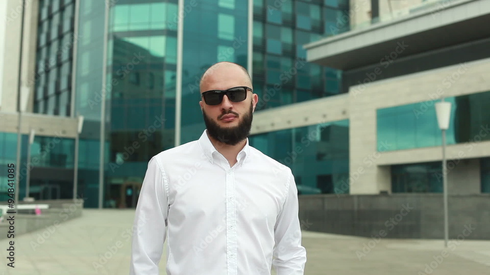 Businessman standing near office building  with beard and taking off sunglasses and smiling in camera