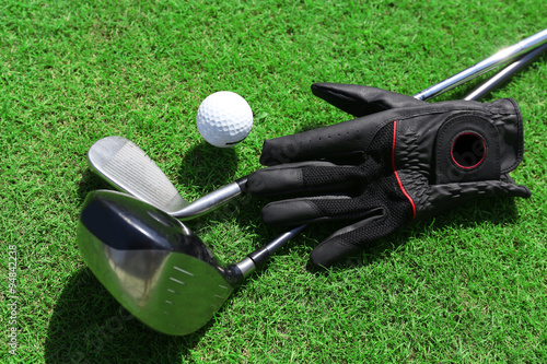 Golf clubs with ball and black glove on a green grass, close up