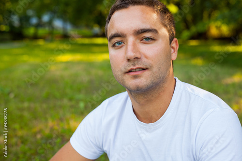 Young man in white shirt is sitting in the park.