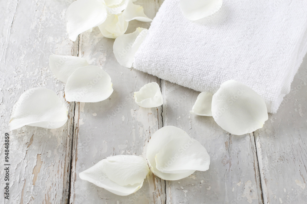 White rose petals and soft towel on a rustic wooden background