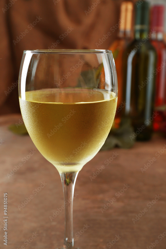 Naklejka premium White wine glass against different bottles and grape on wooden table