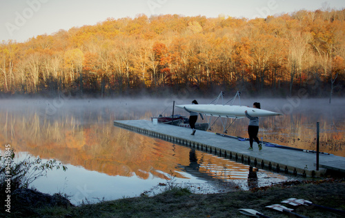 Crew team carries row boat out to the lake during sunrise