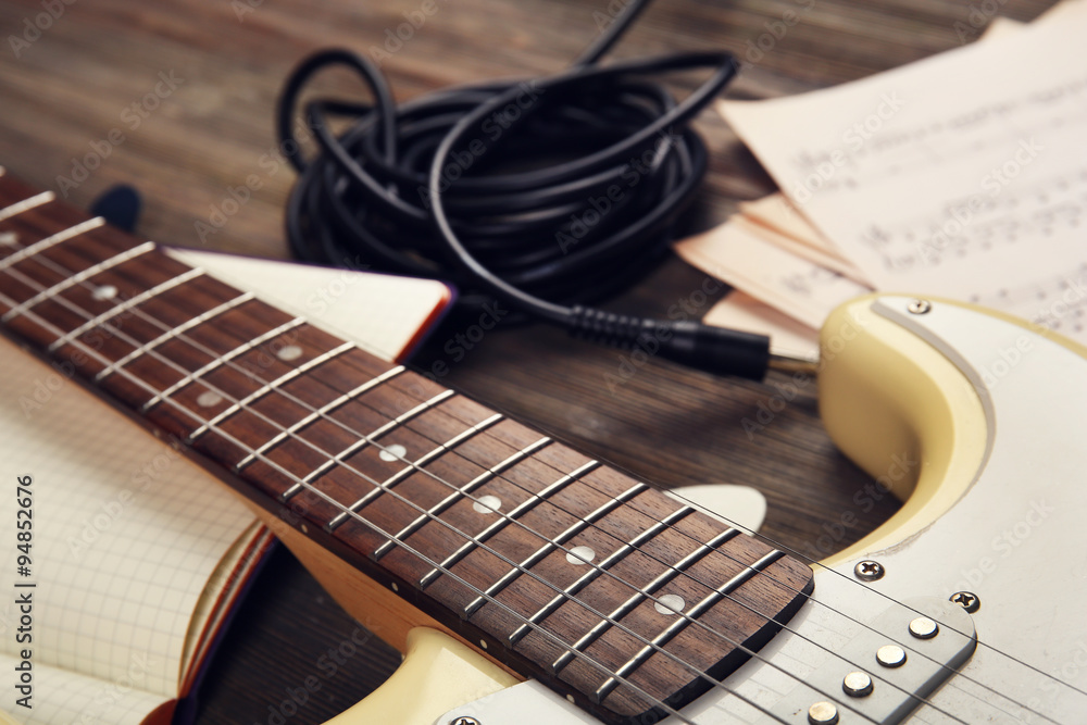 Naklejka premium Electric guitar with musical notes and cord on wooden background