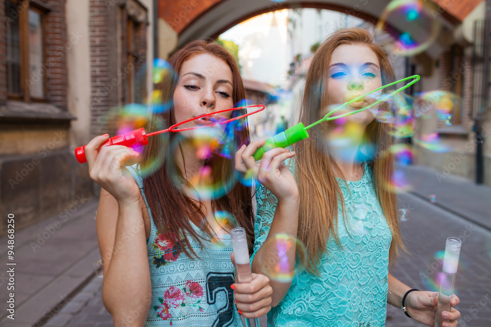 Two pretty girls having fun and blowing bubbles. Urban background.
