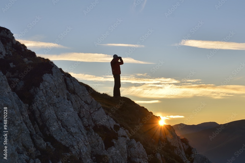 Tourist looking through binoculars sunset in the mountains. Piatra Craiului mountains, Romania.