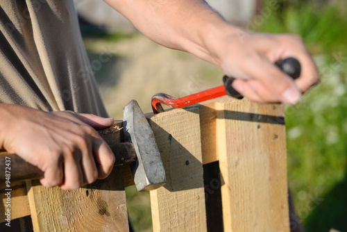 Closeup of hands with crowbar and hammer repairing wooden fence