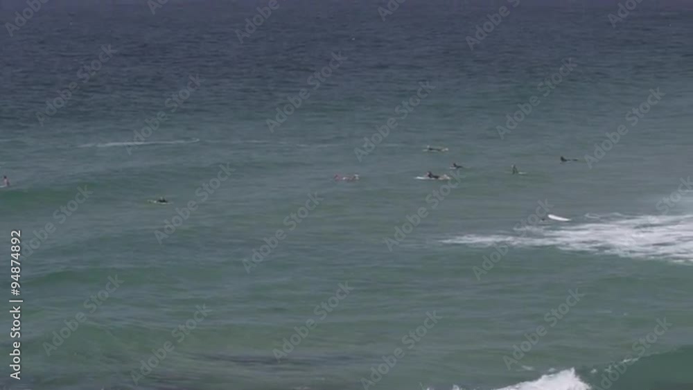 Panning shot of surfers waiting for waves in front of large factory. Panning shot of surfers waiting for waves in front of large factory.