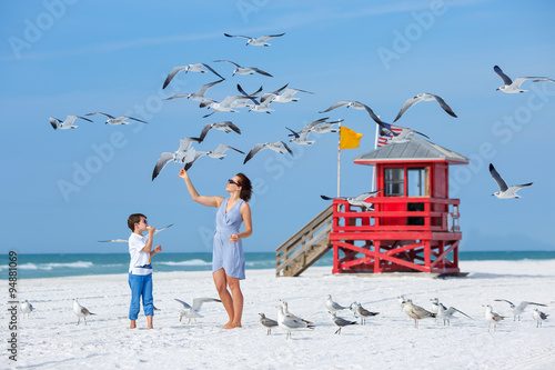 Young mother and her son feeding seagulls on tropical beach