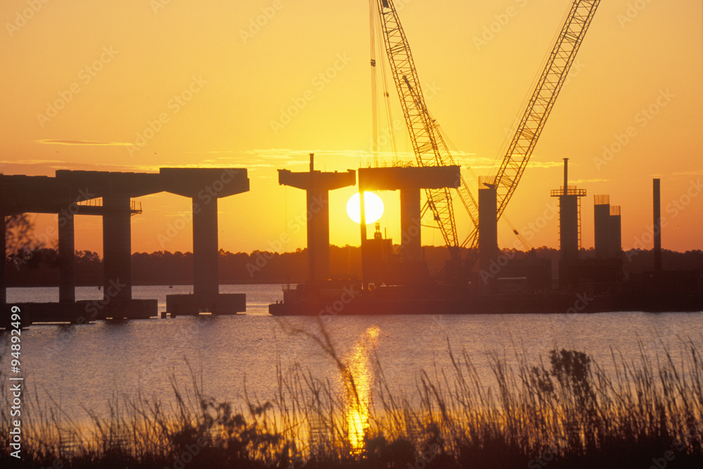 Obraz premium A sun rising behind a bridge building site in New Bern, North Carolina