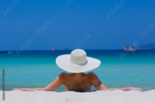 Woman in white hat lying on the beach, blue sea and sky background