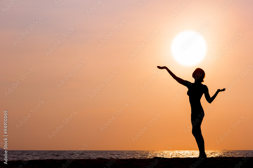 Female silhouette standing on sunset sea background, back lit