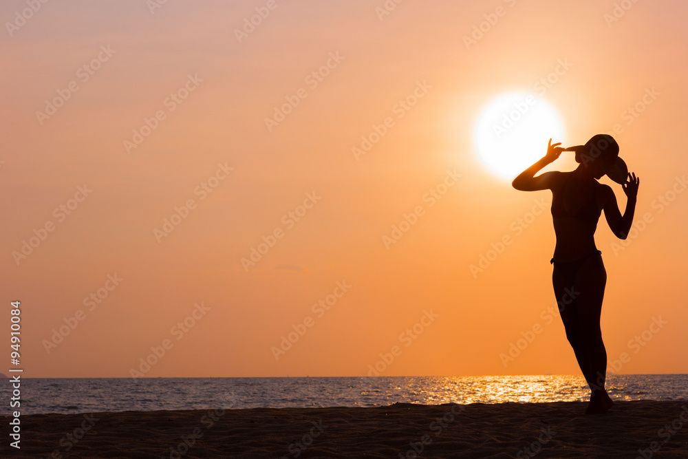 Woman silhouette with hat standing on sunset sea background, back lit