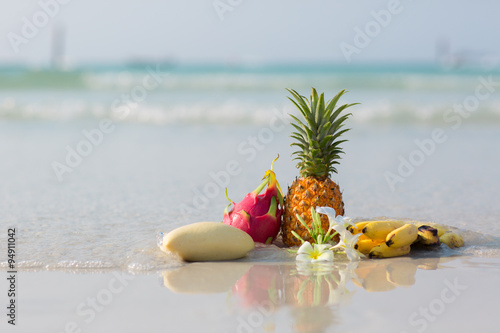 Pineapple, mango, dragon fruit and bananas on the beach on blue sea background