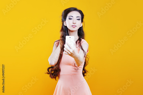Fashion asian young girl taking picture of herself, selfie. Portrait on yellow background