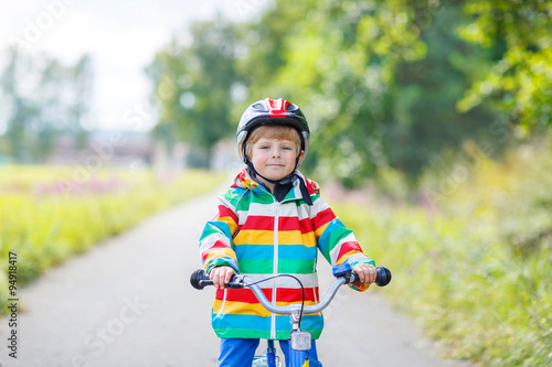 Kid boy in helmet riding his first bike, outdoors