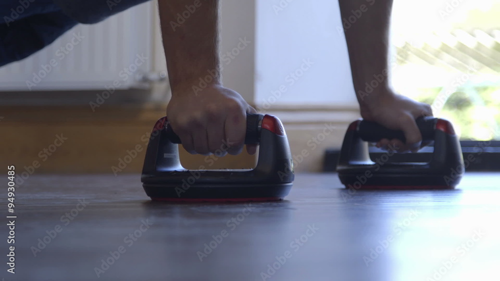 Young man doing press ups in his home using push up bars Young man doing press ups in his home using push up bars