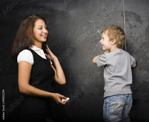 little cute boy in glasses with young real teacher, classroom studying at blackboard school kido close up photo