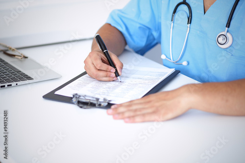 Portrait of unknown male surgeon doctor holding his stethoscope and filling up medical prescription