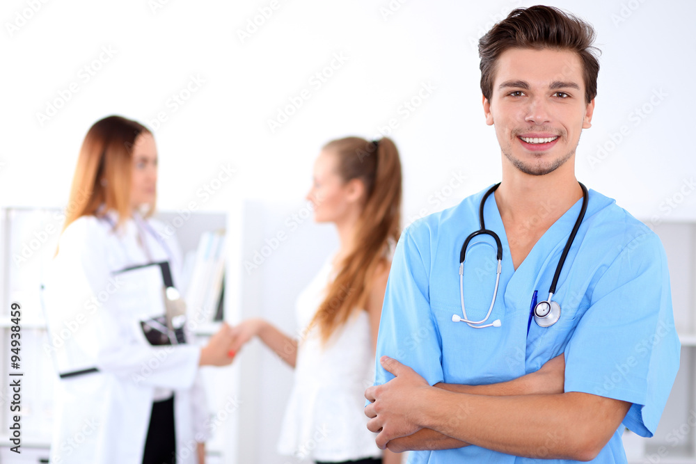 Attractive male doctor in front of medical group, crossed arms Attractive male doctor in front of medical group, crossed arms
