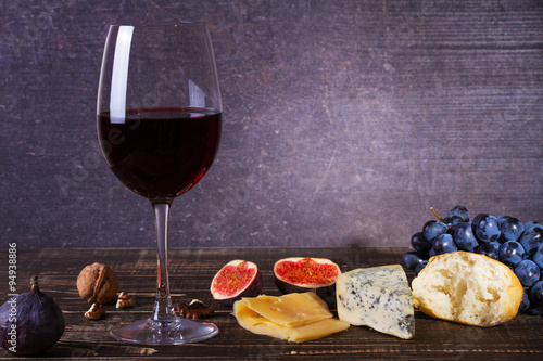 Glass of red wine, cheese, grape, walnuts, figs, plums and apple on wooden background. Still life