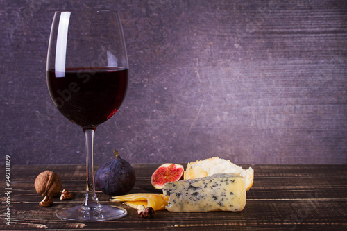 Glass of red wine, cheese, grape, walnuts, figs, plums and apple on wooden background. Still life