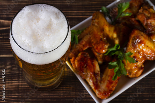 Glass of beer and chicken wings on dark wooden background. View from above, top studio shot