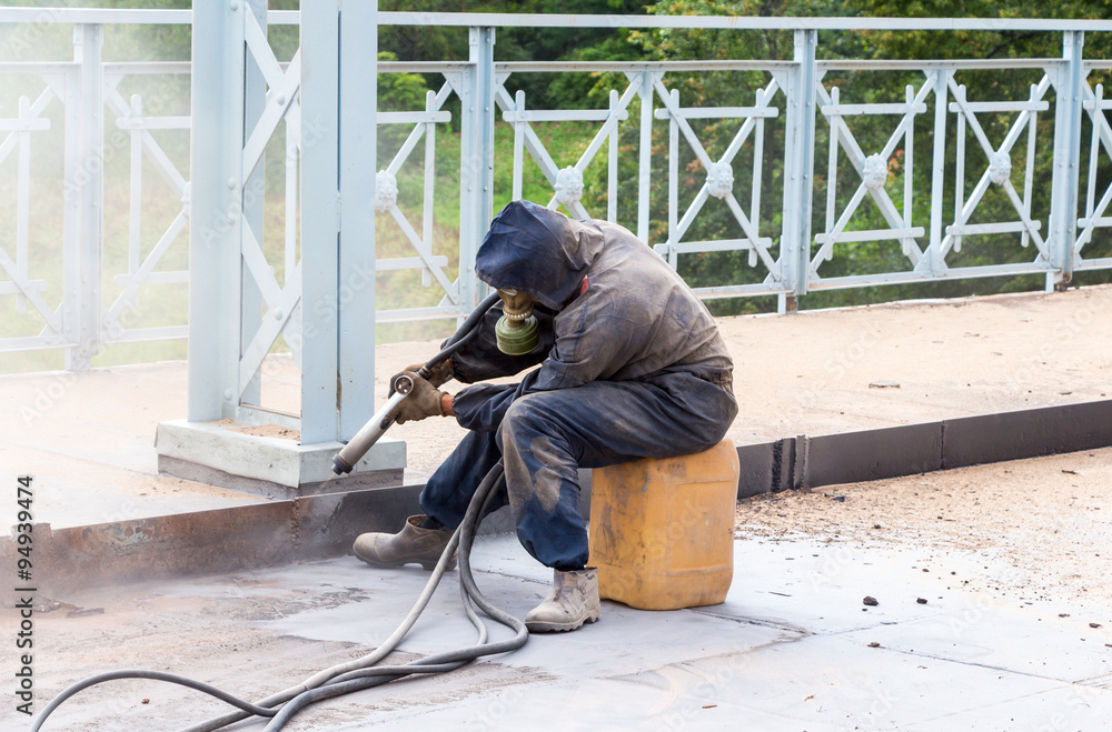 Fotografie Worker in protective clothes cleans the metal structures sandbla