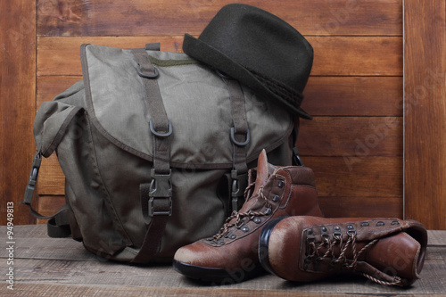 Rucksack with old boots and hat on wooden background
