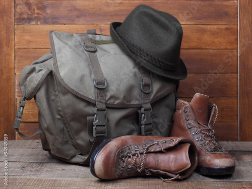 Rucksack with old boots and hat on wooden background