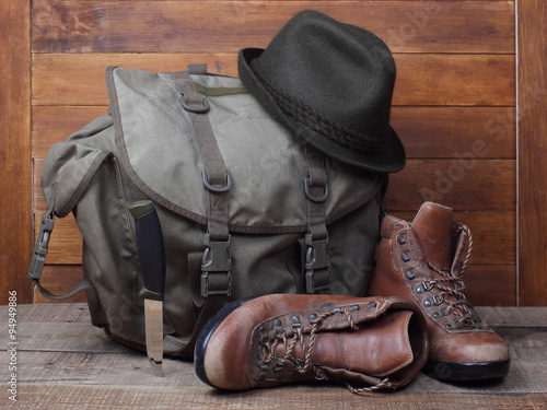 Rucksack with old boots, knife and hat on wooden background