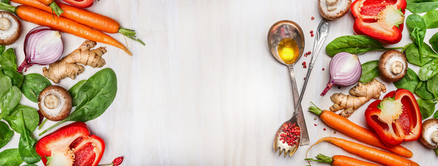 Organic vegetables assorted with cooking spoons and oil on white wooden background