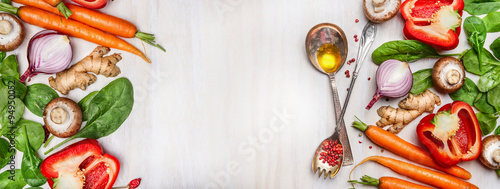 Organic vegetables assorted with cooking spoons and oil on white wooden background