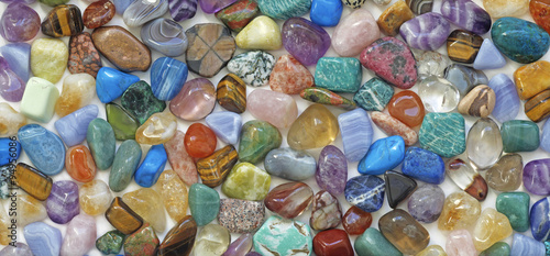 Multicolored tumbled crystal stones background - a large quantity of different colored healing tumbled gem stones making up a backdrop for use as a background photo