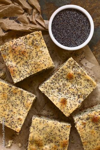 Poppy seed cake pieces on paper with poppy seeds on the side  photographed overhead on slate with natural light