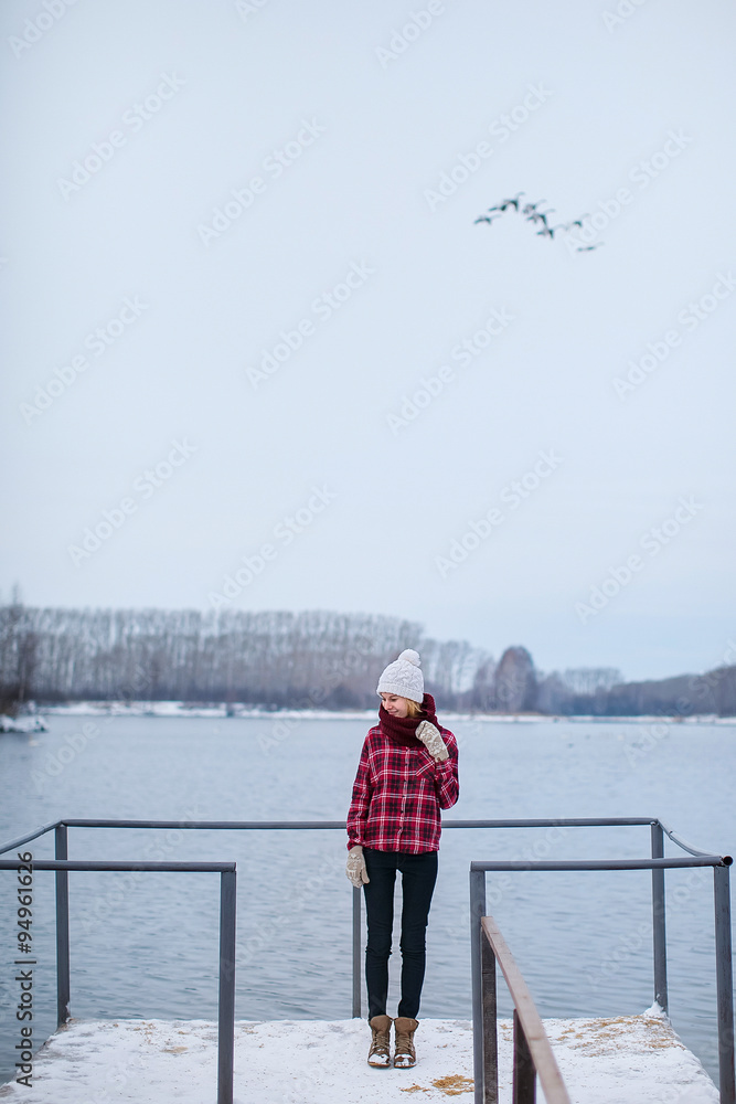 girl in a hat and jacket standing on the dock at the lake in winter girl in a hat and jacket standing on the dock at the lake in winter