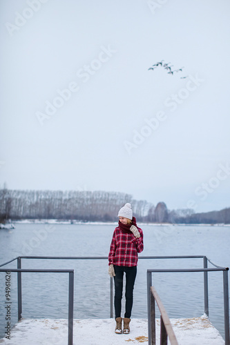 girl in a hat and jacket standing on the dock at the lake in winter