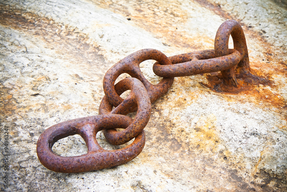 Detail of an old rusty metal chain anchored to a concrete block Detail of an old rusty metal chain anchored to a concrete block