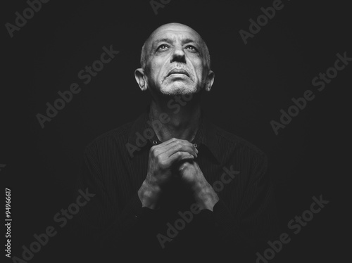Praying senior man looking up with folded hands in the dark