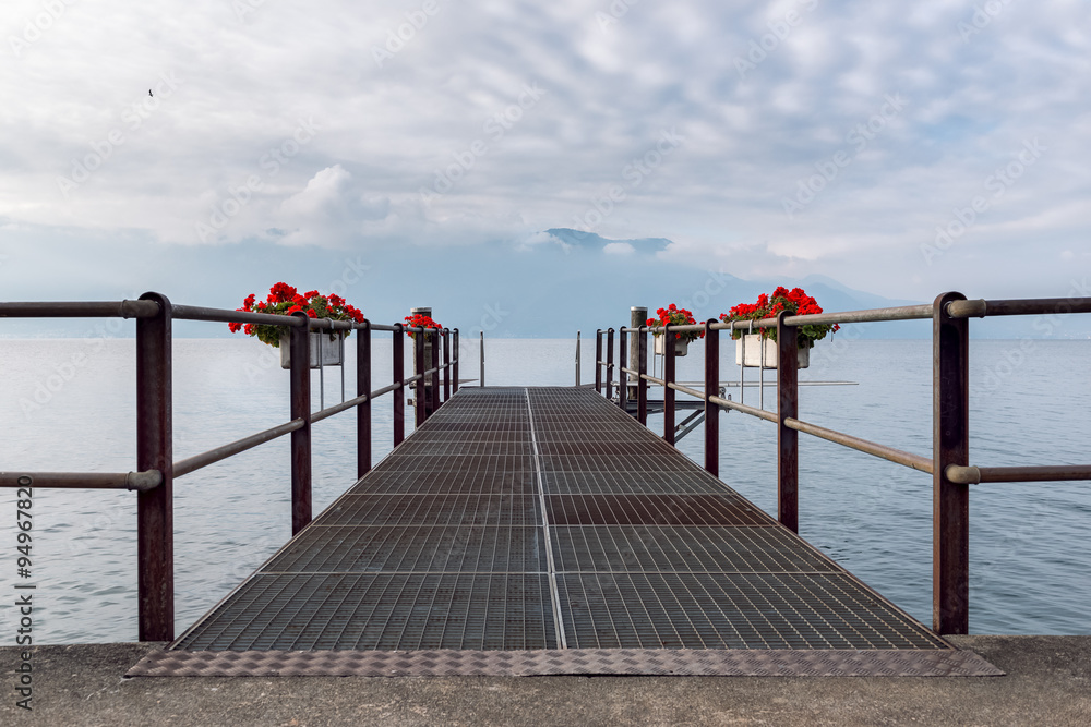 Empty pier flowers decorated on the Geneva lake with view on the French Alps and covered sky.

