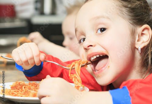 Little girl eat pasta in the kitchen table
