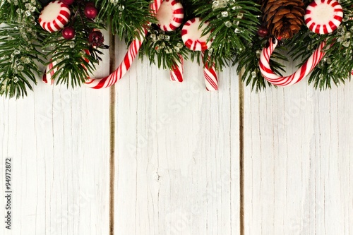 Christmas top border of branches and candy canes against a white wood background