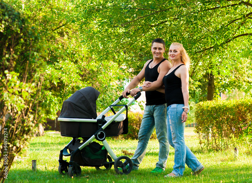 Happy parents pushing baby carriage in the park