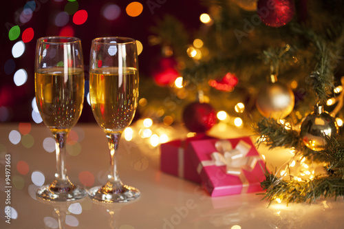 Two glasses of champagne on green christmas tree and gifts 