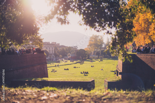 People facing the sunset over the walls surrounding the medieval city of Lucca, Italy, vintage with grain and blurred effect with flare