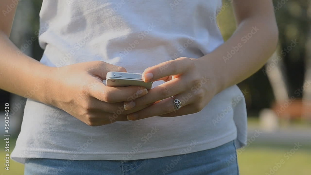 Girl sms texting using app on smart phone in a park. Girl sms texting using app on smart phone in a park.