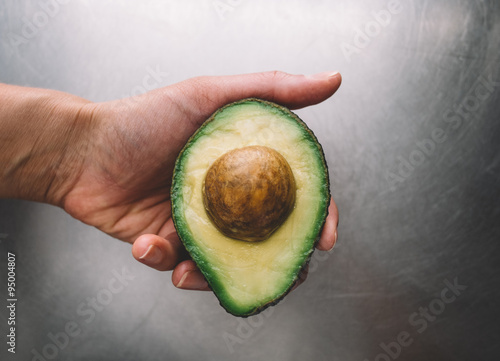 Half an avocado in a hand on the background of a steel table top view
