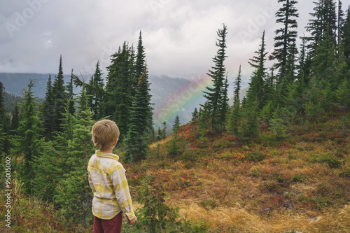 Rear view of a boy standing on mountain looking at rainbow