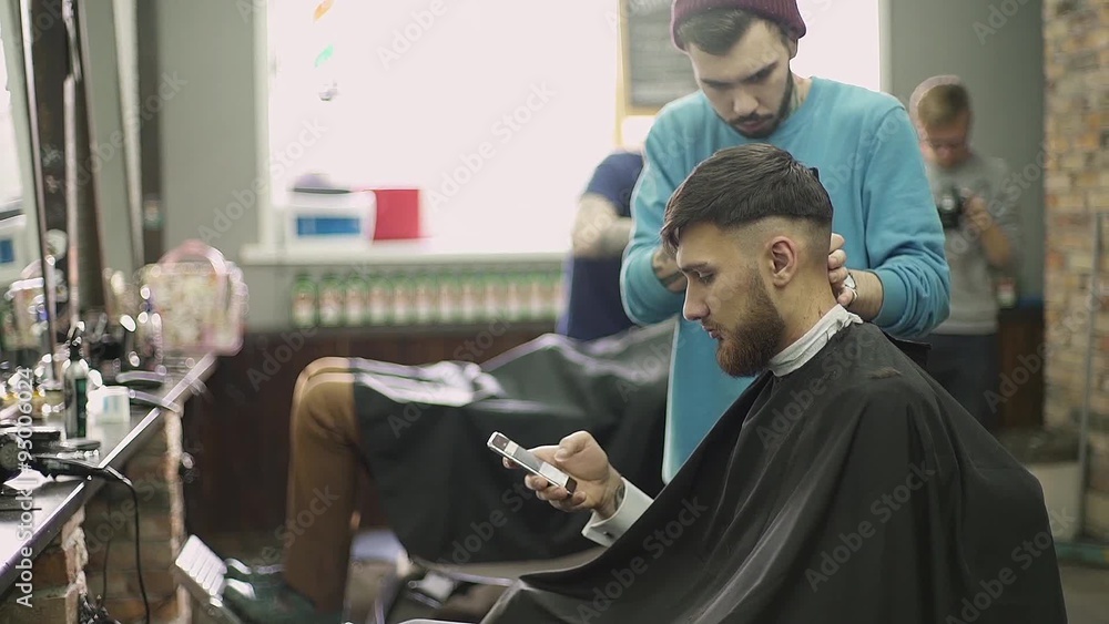 Young man using a smart phone in barber shop Young man using a smart phone in barber shop