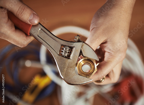 Slika na platnu Close-up of plumber hands screwing nut of pipe with wrench over plumbing tools background
